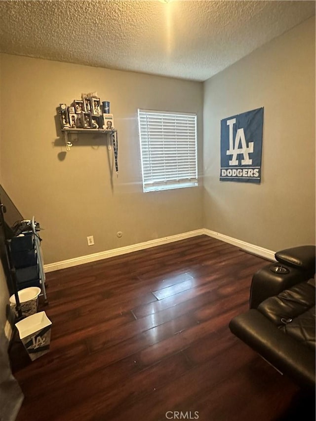 living area with baseboards, a textured ceiling, and wood finished floors