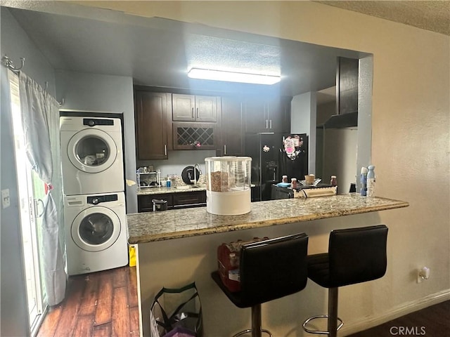 kitchen featuring a breakfast bar area, dark wood-style flooring, stacked washer / drying machine, light stone counters, and a peninsula