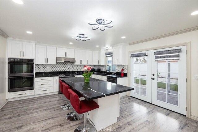 12246 Nadine Cir, Garden Grove, CA 92840 - kitchen featuring french doors, light wood-type flooring, tasteful backsplash, under cabinet range hood, and black appliances