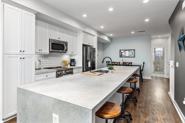 kitchen with a kitchen island with sink, dark wood-type flooring, white cabinetry, a sink, and appliances with stainless steel finishes