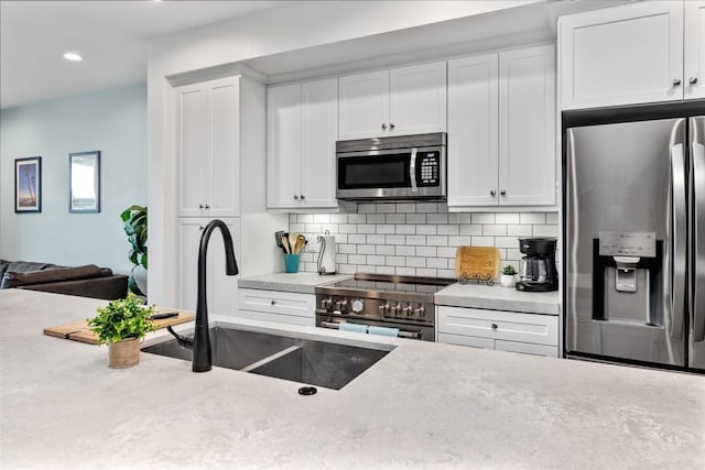 kitchen featuring white cabinetry, appliances with stainless steel finishes, decorative backsplash, and a sink
