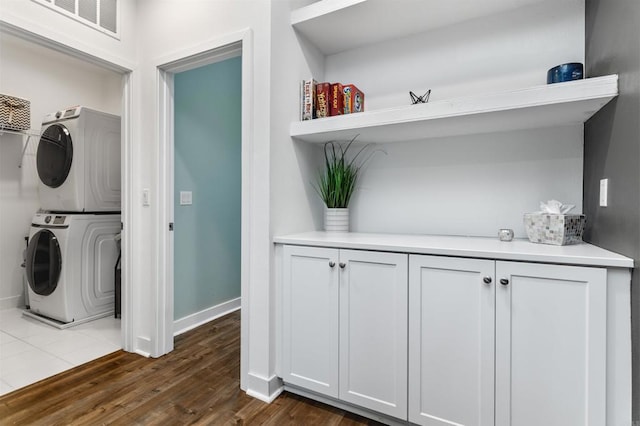 washroom with dark wood-style flooring, stacked washer and dryer, laundry area, baseboards, and visible vents