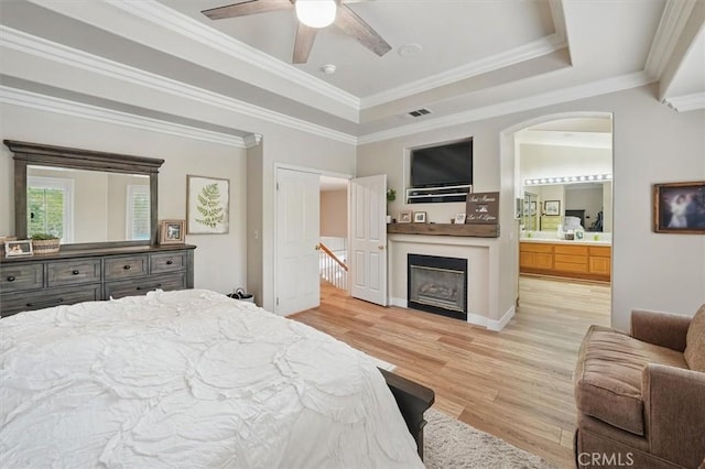 bedroom featuring light wood finished floors, a tray ceiling, a fireplace, visible vents, and arched walkways