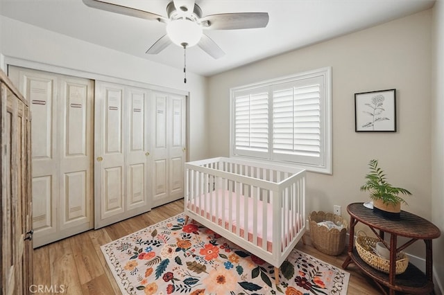 bedroom featuring light wood finished floors, a closet, a crib, and ceiling fan