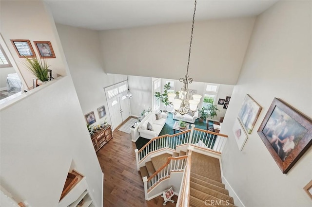staircase with a chandelier, wood finished floors, baseboards, and high vaulted ceiling