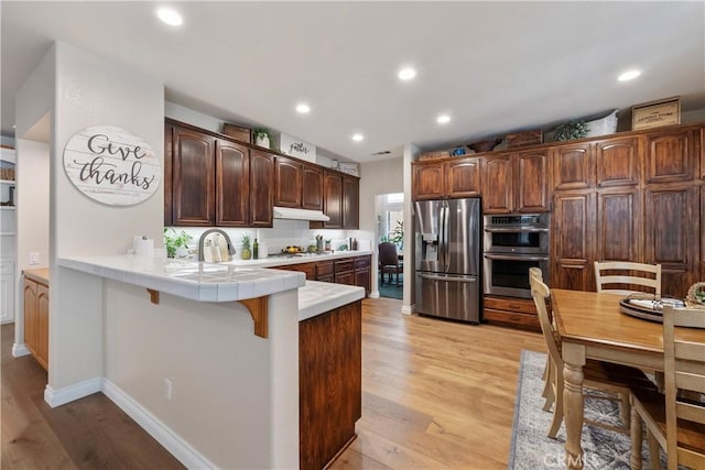 28433 Pinewood Ct, Saugus, CA 91390 - kitchen featuring stainless steel appliances, a peninsula, tile countertops, light wood finished floors, and under cabinet range hood