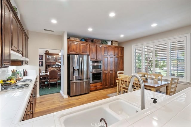 28433 Pinewood Ct, Saugus, CA 91390 - kitchen with appliances with stainless steel finishes, tile counters, light wood-style flooring, under cabinet range hood, and recessed lighting