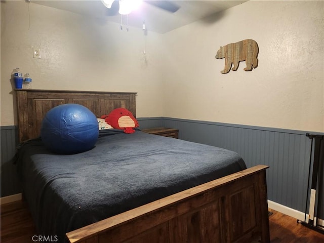bedroom with a wainscoted wall, wood finished floors, and ceiling fan