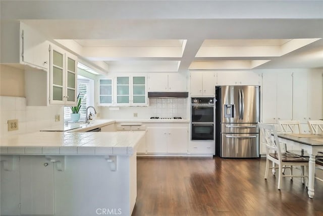 kitchen featuring dobule oven black, a peninsula, dark wood-style floors, stainless steel fridge, and under cabinet range hood