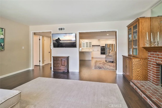 living area with baseboards, visible vents, dark wood finished floors, and a fireplace