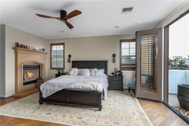 bedroom with visible vents, access to exterior, wood finished floors, baseboards, and a glass covered fireplace