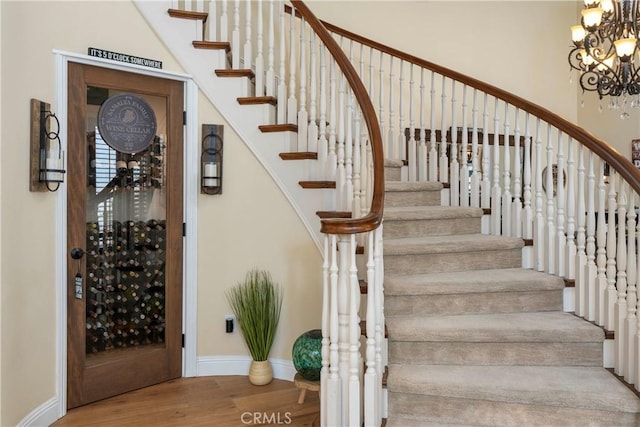 stairway featuring baseboards, a chandelier, and wood finished floors