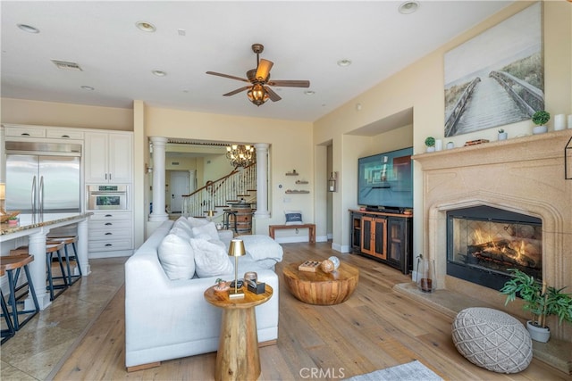 living room featuring a ceiling fan, light wood-type flooring, a high end fireplace, visible vents, and stairway