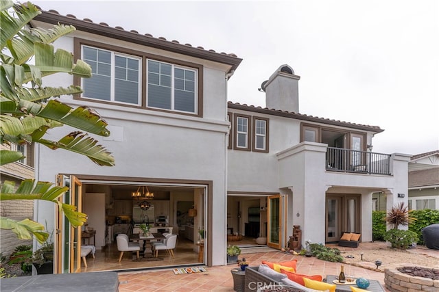 back of house with a chimney, a balcony, a patio, a fire pit, and stucco siding