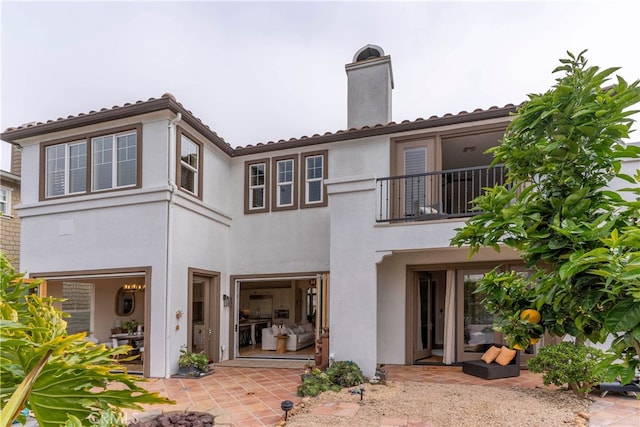 rear view of house with a chimney, a balcony, a patio area, and stucco siding