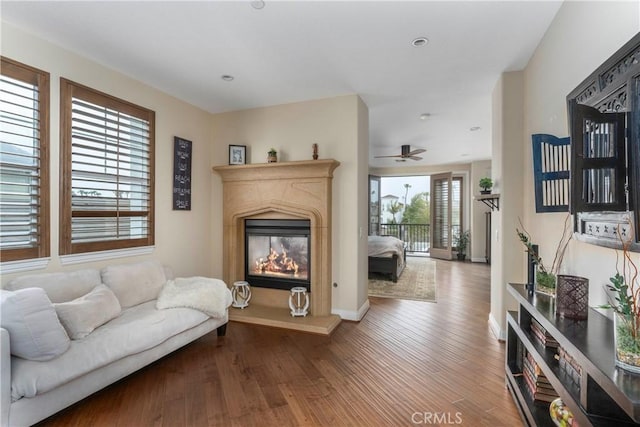 living room with baseboards, a ceiling fan, a glass covered fireplace, and wood finished floors