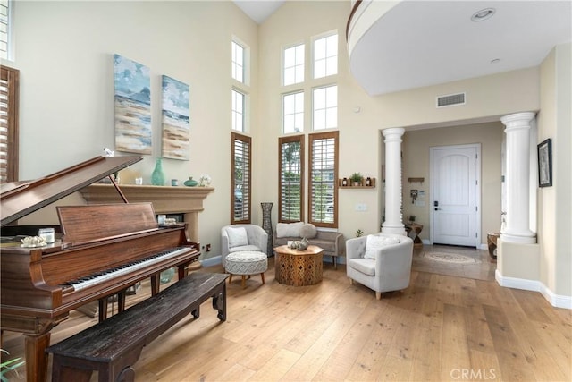 living area with light wood-style floors, decorative columns, a towering ceiling, and visible vents