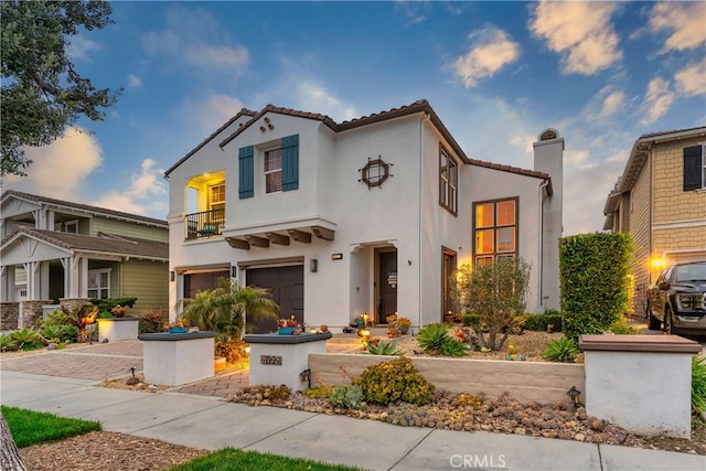 mediterranean / spanish home with an attached garage, stucco siding, a balcony, a tiled roof, and driveway