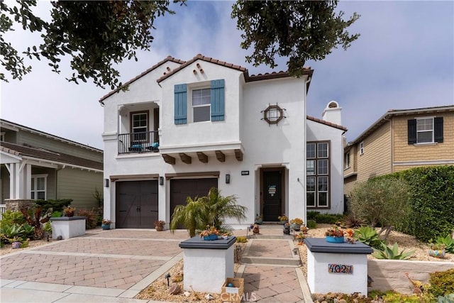 mediterranean / spanish house featuring a tiled roof, stucco siding, an attached garage, and decorative driveway