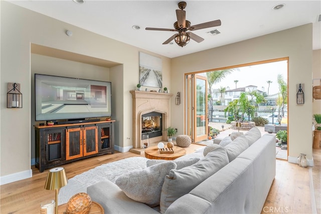 living room featuring a glass covered fireplace, a ceiling fan, wood finished floors, and visible vents
