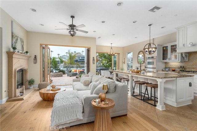 living room with light wood-style floors, a glass covered fireplace, ceiling fan with notable chandelier, recessed lighting, and visible vents