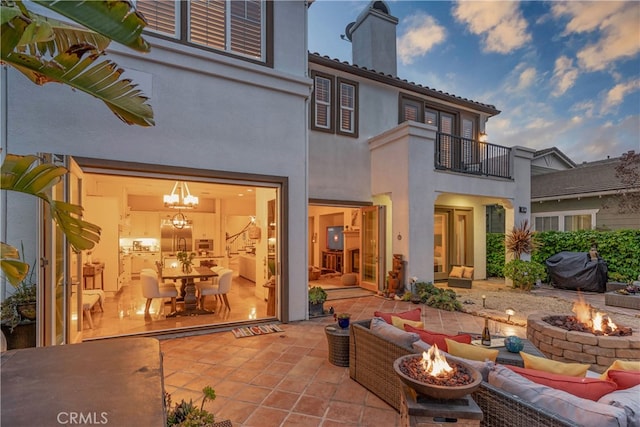 back of property with an outdoor living space with a fire pit, a balcony, a patio, stucco siding, and a chimney