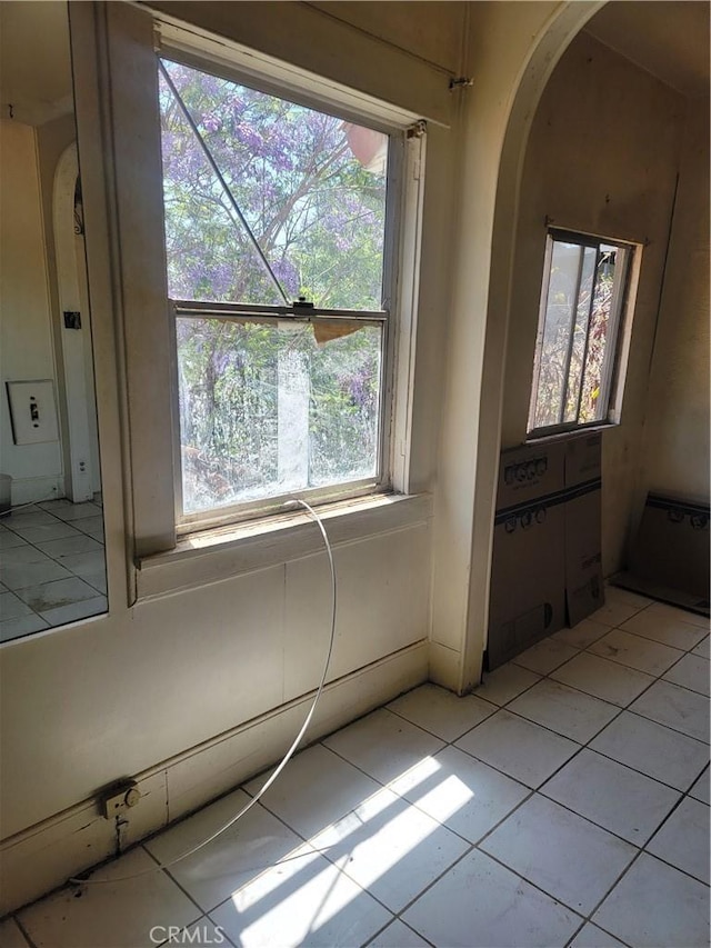unfurnished room with arched walkways, plenty of natural light, and light tile patterned flooring