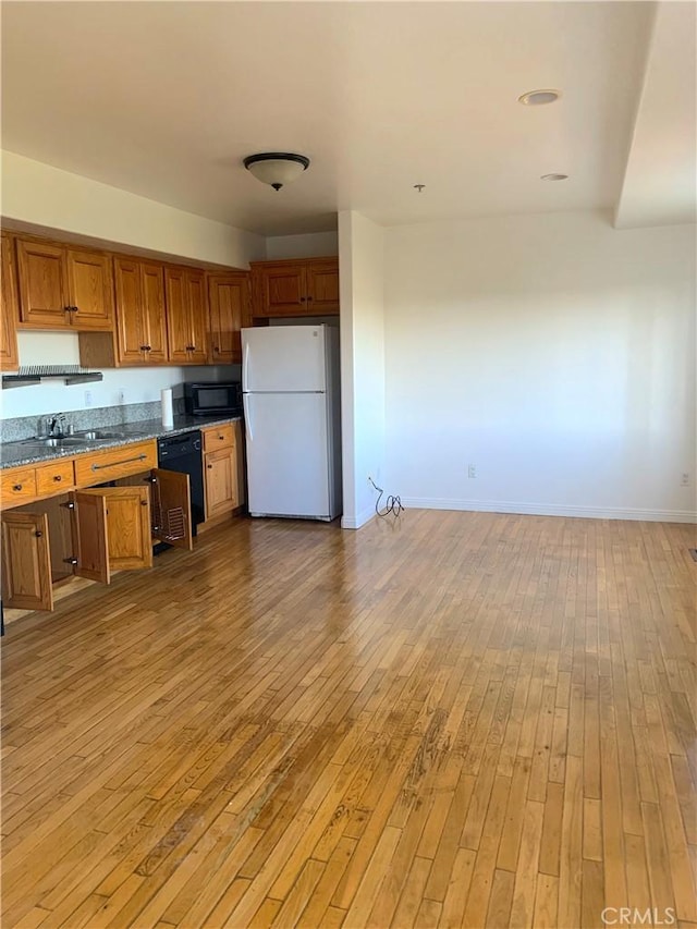 kitchen featuring brown cabinets, light wood-style flooring, a sink, dark countertops, and black appliances