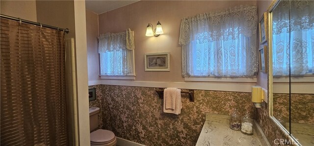 bathroom featuring toilet, a shower with shower curtain, and a wainscoted wall