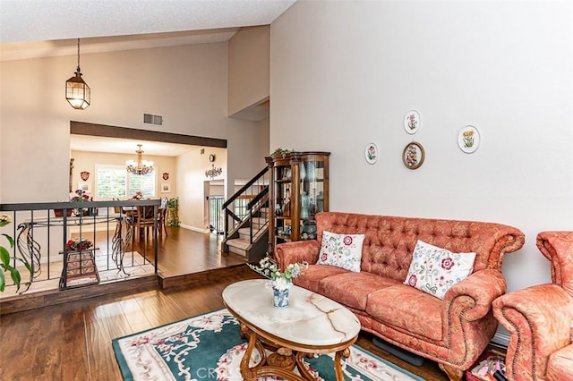 living area featuring visible vents, wood finished floors, stairway, high vaulted ceiling, and an inviting chandelier