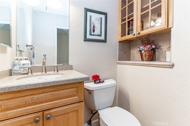 bathroom featuring backsplash, toilet, a textured wall, and vanity