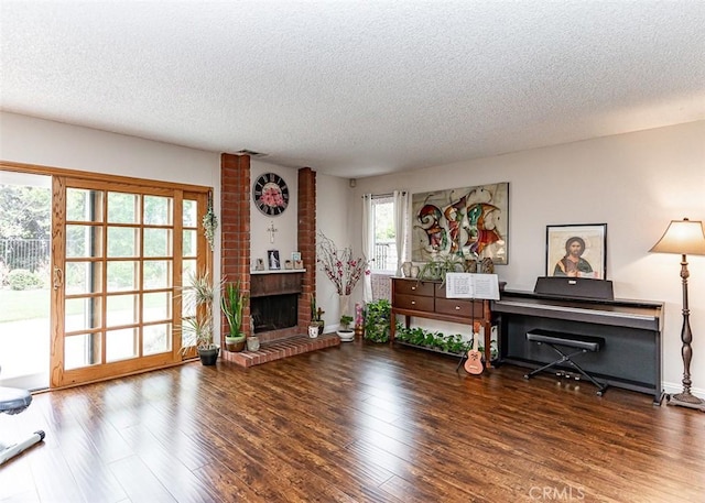 sitting room with a brick fireplace, a textured ceiling, and wood finished floors