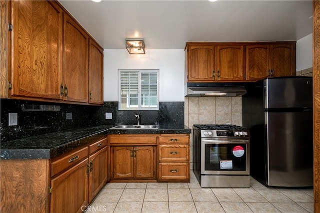 kitchen with brown cabinets, appliances with stainless steel finishes, a sink, light tile patterned floors, and under cabinet range hood