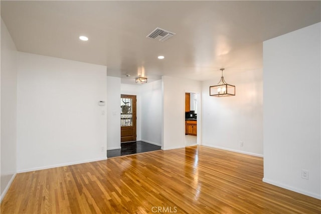spare room featuring visible vents, baseboards, wood finished floors, and a notable chandelier
