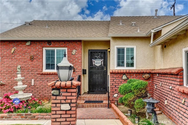property entrance with roof with shingles, stucco siding, and brick siding