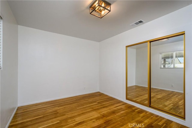 unfurnished bedroom with visible vents, baseboards, wood finished floors, and a closet