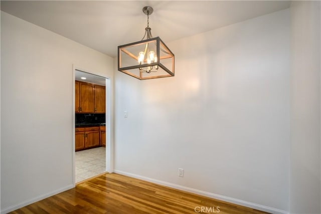 unfurnished dining area with baseboards, a chandelier, and light wood finished floors