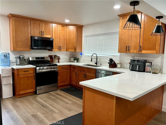 kitchen with brown cabinets, appliances with stainless steel finishes, a sink, a peninsula, and recessed lighting