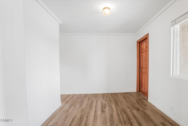 spare room with crown molding, light wood-style flooring, and baseboards
