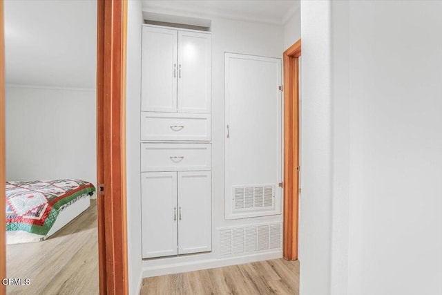 hall with crown molding, light wood-style floors, and visible vents
