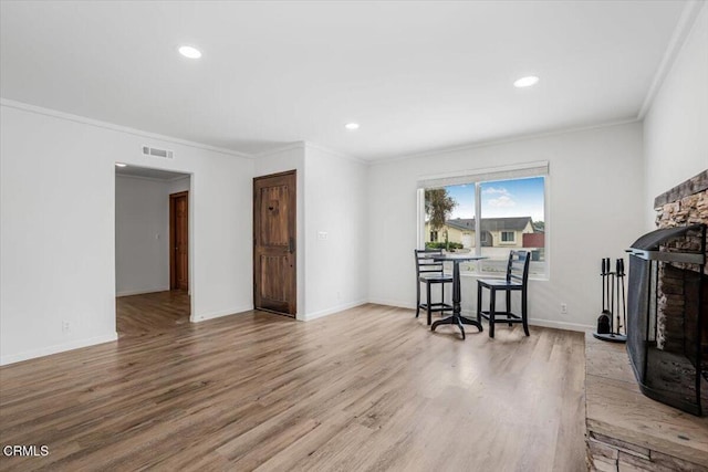 living area featuring a stone fireplace, ornamental molding, visible vents, and wood finished floors