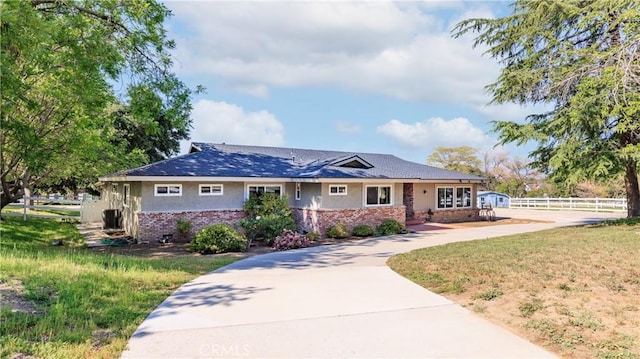 ranch-style house featuring a front lawn, brick siding, driveway, and fence