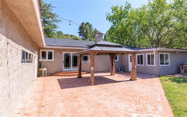 rear view of house featuring stucco siding, a chimney, a gazebo, and a patio