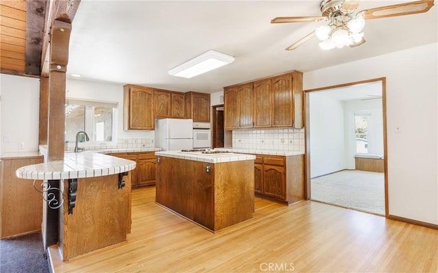 kitchen featuring brown cabinetry, tile counters, white appliances, and light wood-style flooring