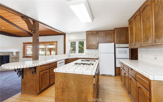 kitchen featuring tile countertops, white appliances, light wood finished floors, a peninsula, and backsplash