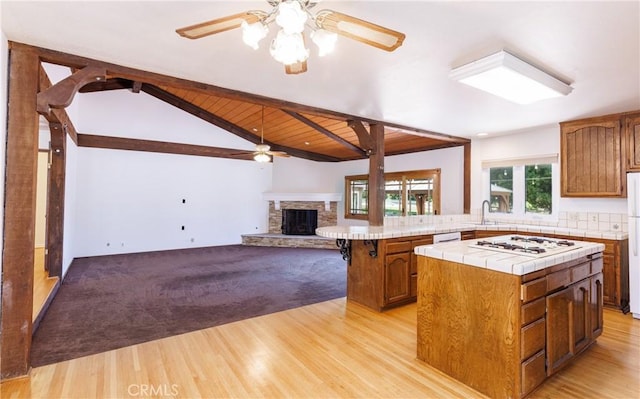 kitchen featuring brown cabinets, a fireplace, tile counters, ceiling fan, and white appliances