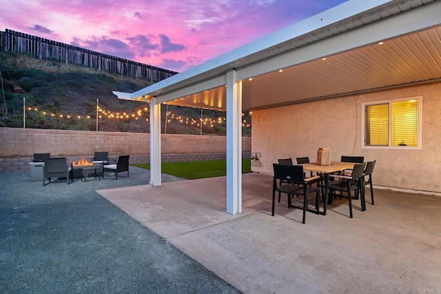 patio terrace at dusk featuring outdoor dining area, a fire pit, and a fenced backyard