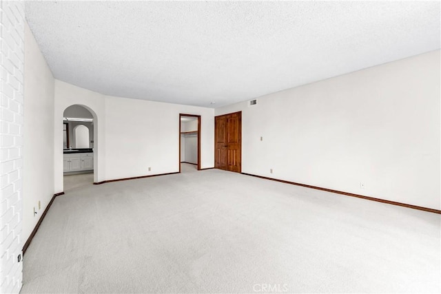 unfurnished room with light colored carpet, a textured ceiling, visible vents, arched walkways, and baseboards