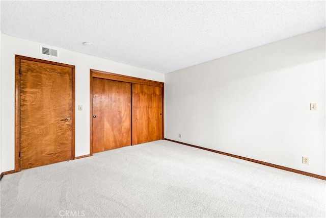unfurnished bedroom featuring carpet, a textured ceiling, visible vents, and a closet