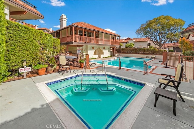 community pool featuring fence, a community hot tub, and a patio area